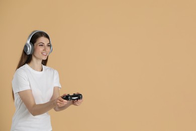 Happy woman in headphones playing video games with controller on beige background, space for text