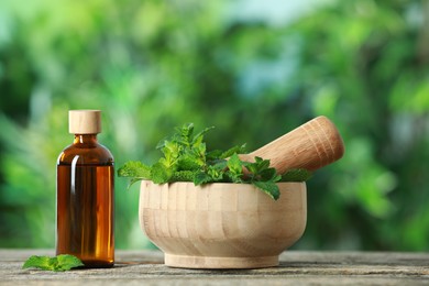 Bottle of mint essential oil and leaves on wooden table against blurred background