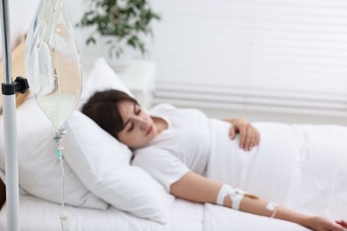Young woman with intravenous drip in hospital bed, selective focus