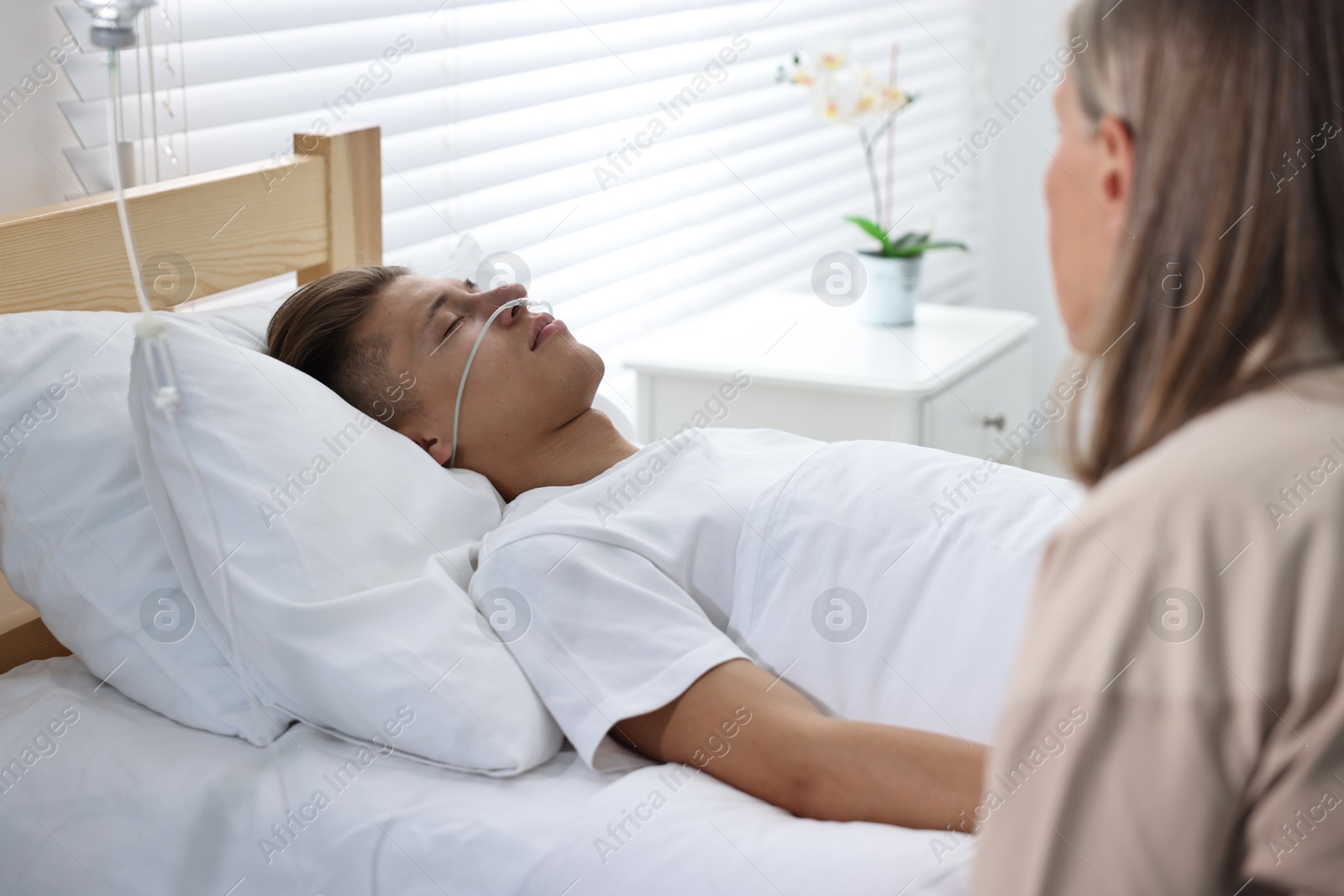 Photo of Coma patient. Sad mature woman near her unconscious son in hospital