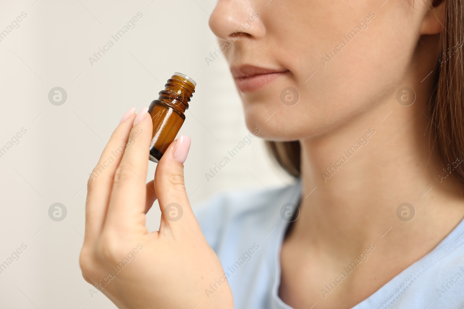 Photo of Aromatherapy. Woman with bottle of essential oil on light background, closeup