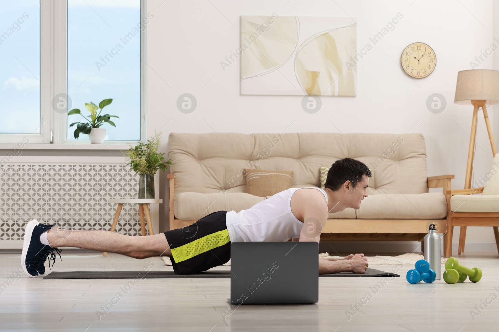 Photo of Online fitness trainer. Man doing plank exercise near laptop at home