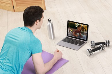 Photo of Online fitness trainer. Man doing plank exercise near laptop at home