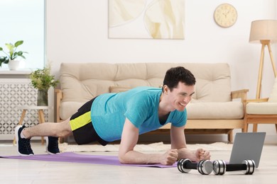 Online fitness trainer. Man doing plank exercise near laptop at home