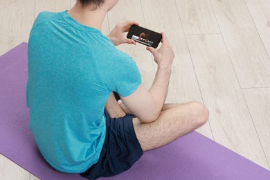 Online fitness trainer. Man watching tutorial on smartphone indoors, closeup. Space for text
