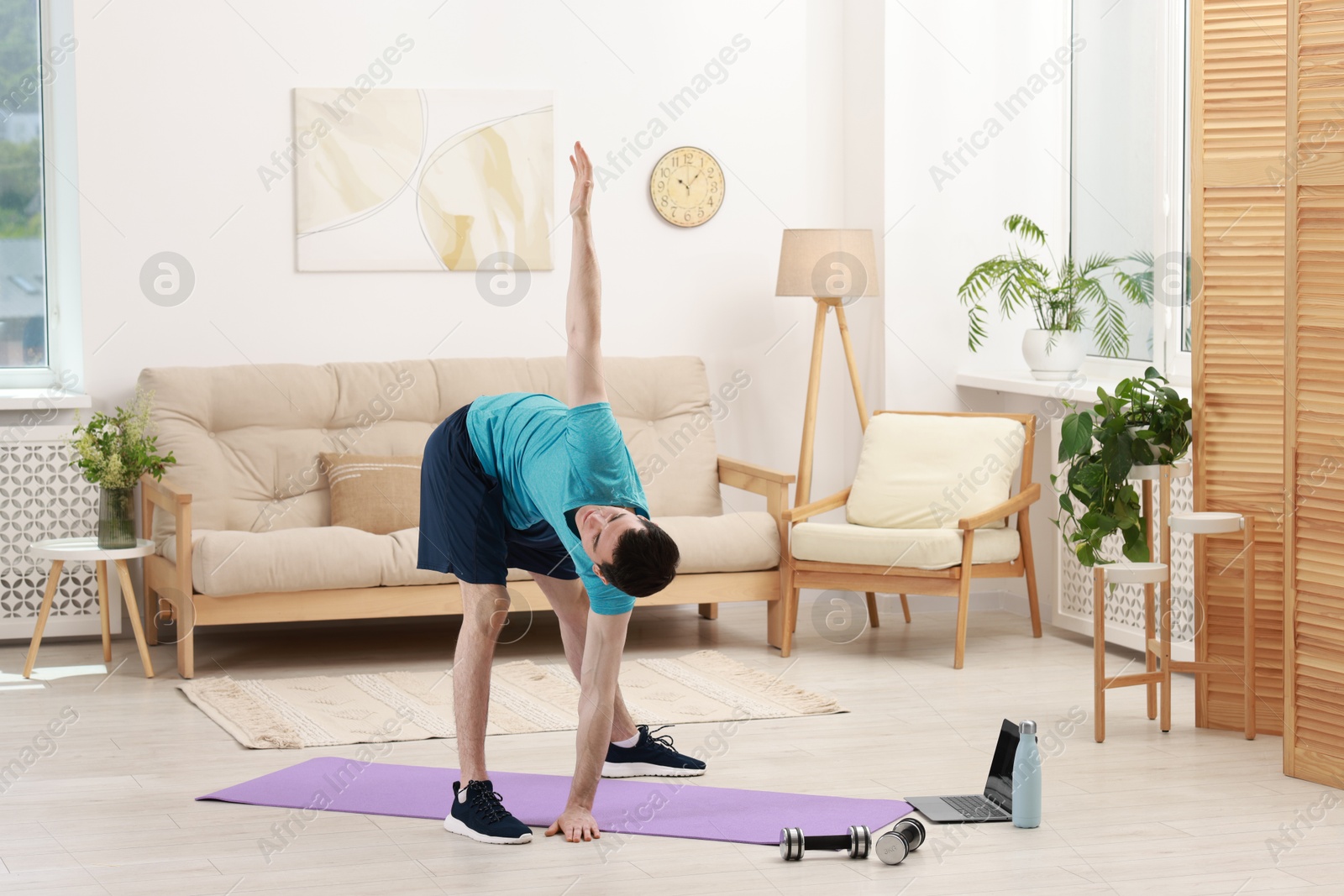 Photo of Online fitness trainer. Man doing exercise near laptop at home