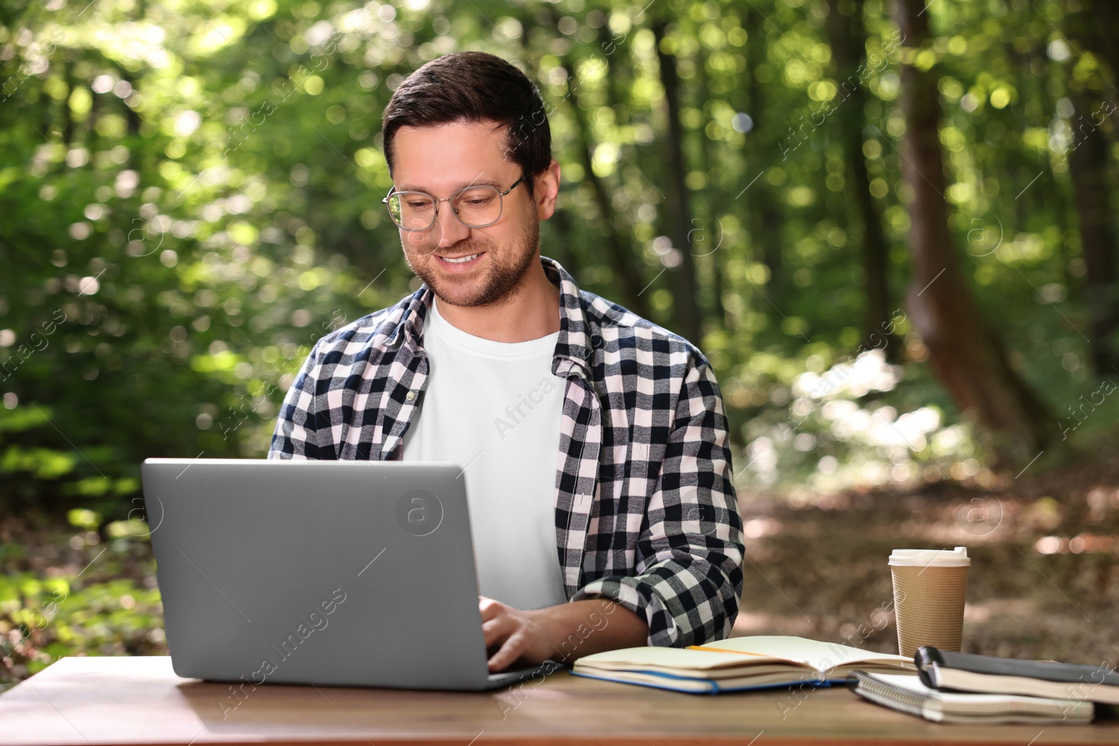 Photo of Smiling freelancer working with laptop at table outdoors. Remote job