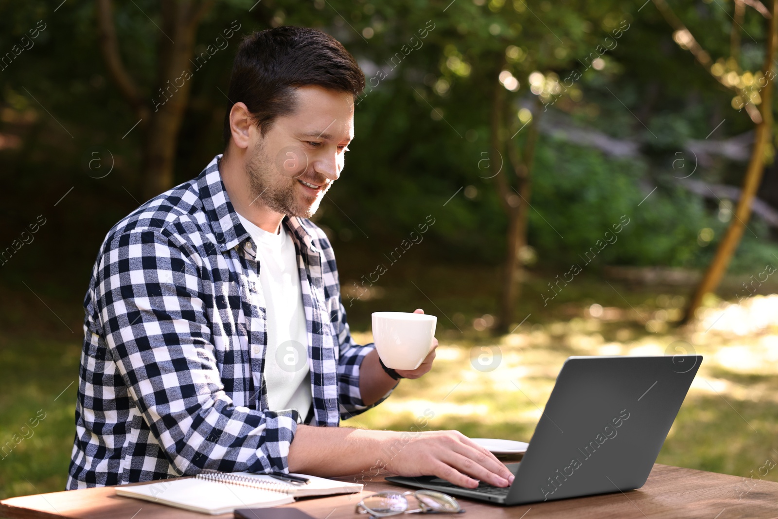 Photo of Smiling freelancer working with laptop at table outdoors. Remote job