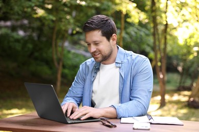 Photo of Smiling freelancer working with laptop at table outdoors. Remote job