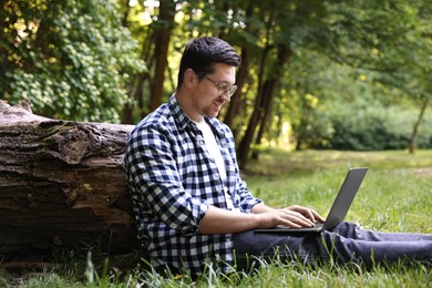 Photo of Smiling freelancer working with laptop on green grass in forest. Remote job