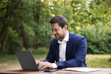 Smiling businessman working with laptop at table outdoors. Remote job