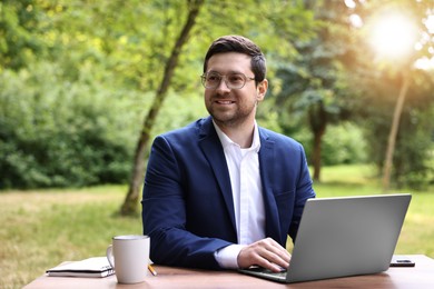 Smiling businessman working with laptop at table outdoors. Remote job