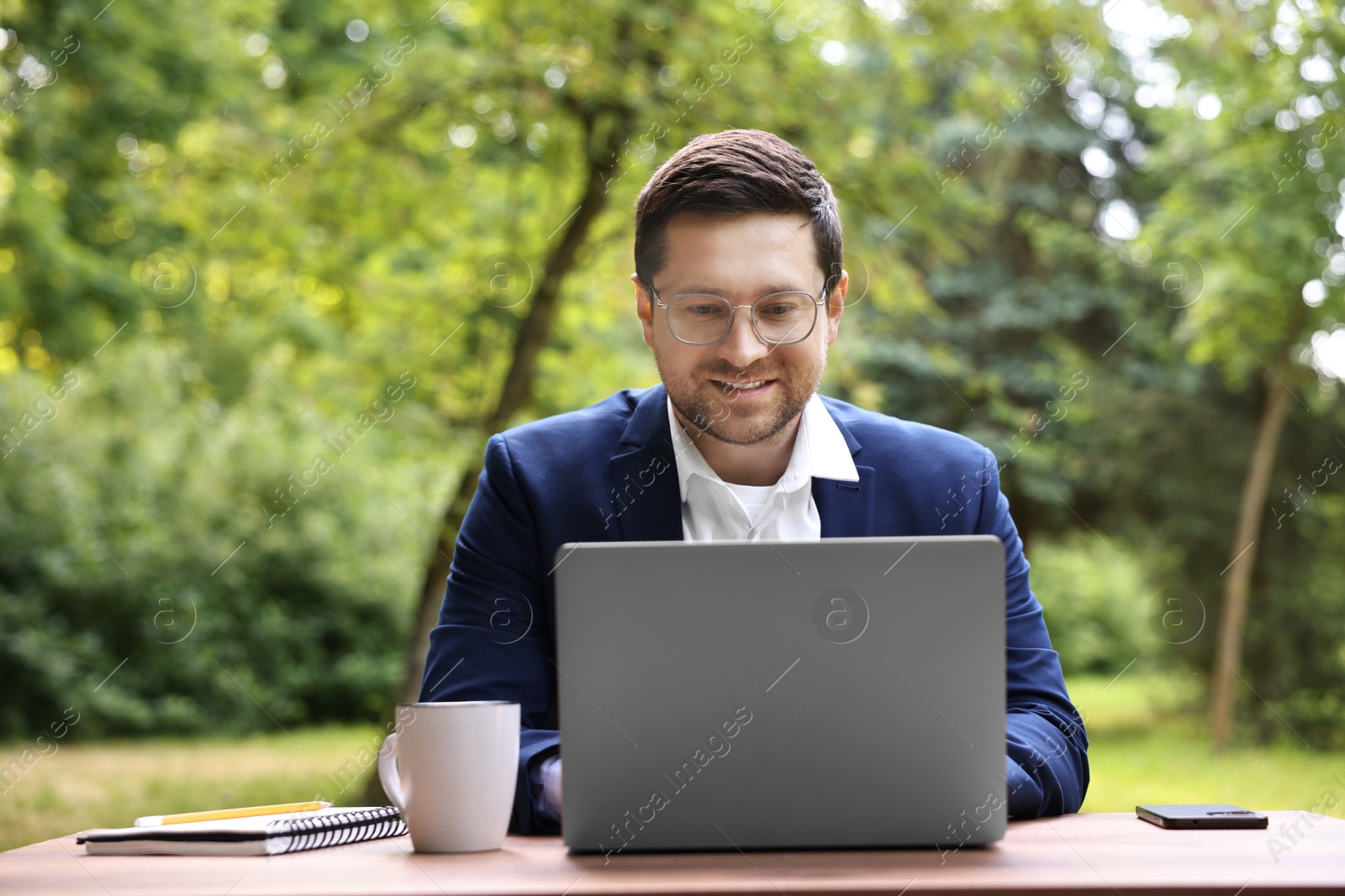 Photo of Smiling businessman working with laptop at table outdoors. Remote job