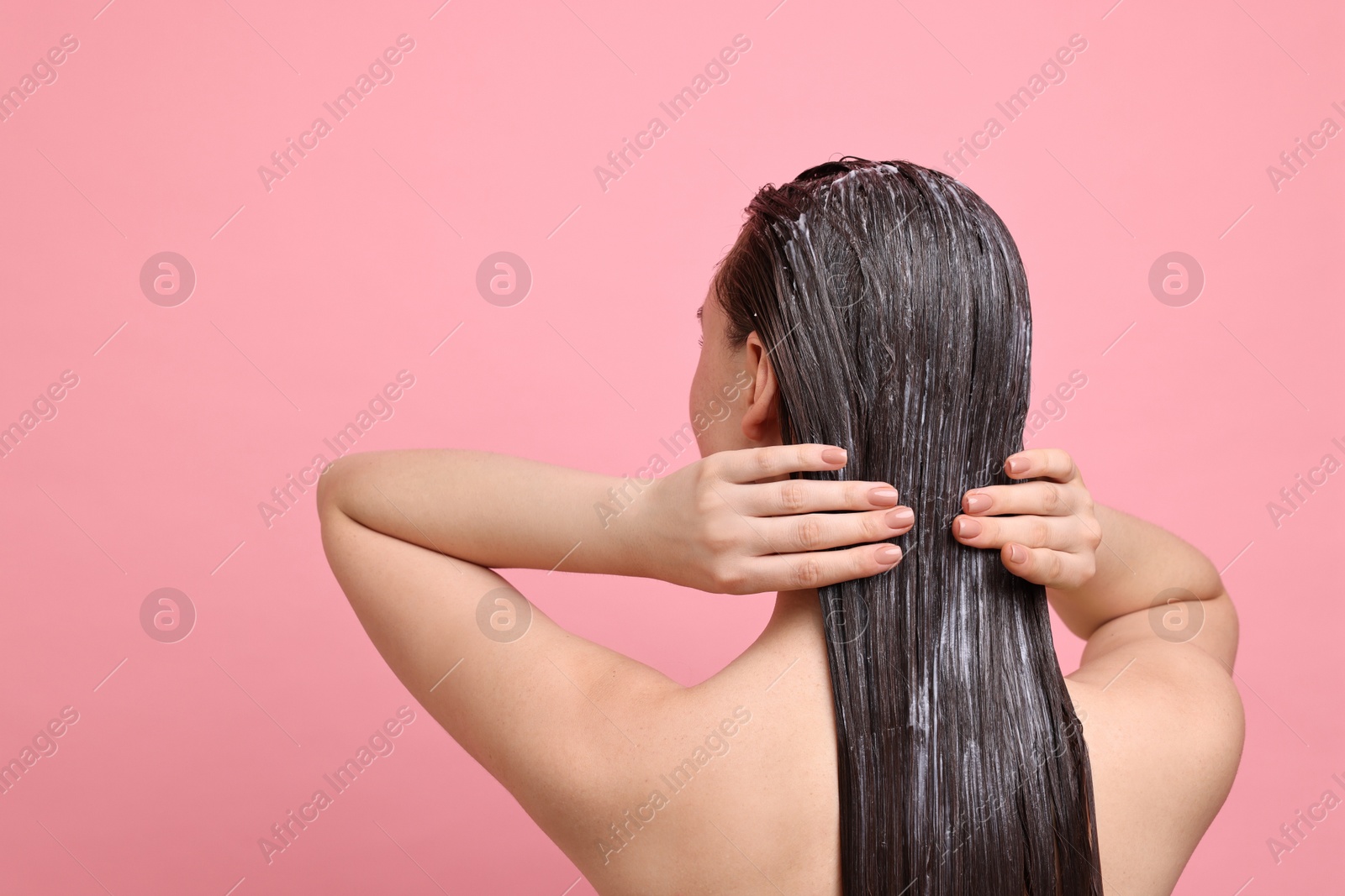 Photo of Woman applying hair mask on pink background, back view. Space for text