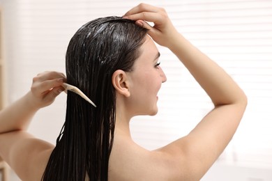 Woman combing her hair with applied mask in bathroom, back view