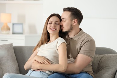 Photo of Man hugging his happy girlfriend on sofa at home