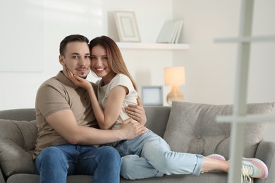 Photo of Man hugging his happy girlfriend on sofa at home