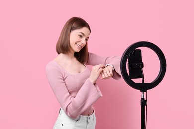 Photo of Fashion blogger reviewing watch and recording video with smartphone and ring lamp on pink background