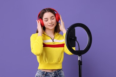 Technology blogger reviewing headphones and recording video with smartphone and ring lamp on purple background