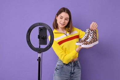 Photo of Fashion blogger reviewing sneakers and recording video with smartphone and ring lamp on purple background