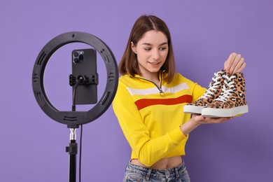 Photo of Fashion blogger reviewing sneakers and recording video with smartphone and ring lamp on purple background