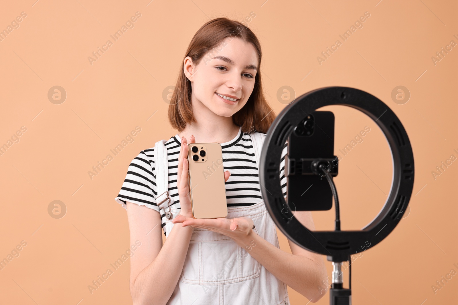 Photo of Technology blogger reviewing phone and recording video with smartphone and ring lamp on beige background