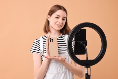 Technology blogger reviewing phone and recording video with smartphone and ring lamp on beige background