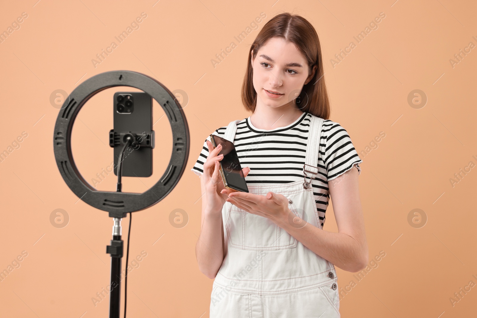 Photo of Technology blogger reviewing phone and recording video with smartphone and ring lamp on beige background