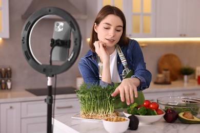 Food blogger cooking while recording video with smartphone and ring lamp in kitchen