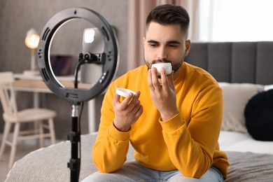 Beauty blogger reviewing cosmetic product and recording video with smartphone and ring lamp at home