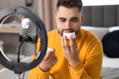 Beauty blogger reviewing cosmetic product and recording video with smartphone and ring lamp at home