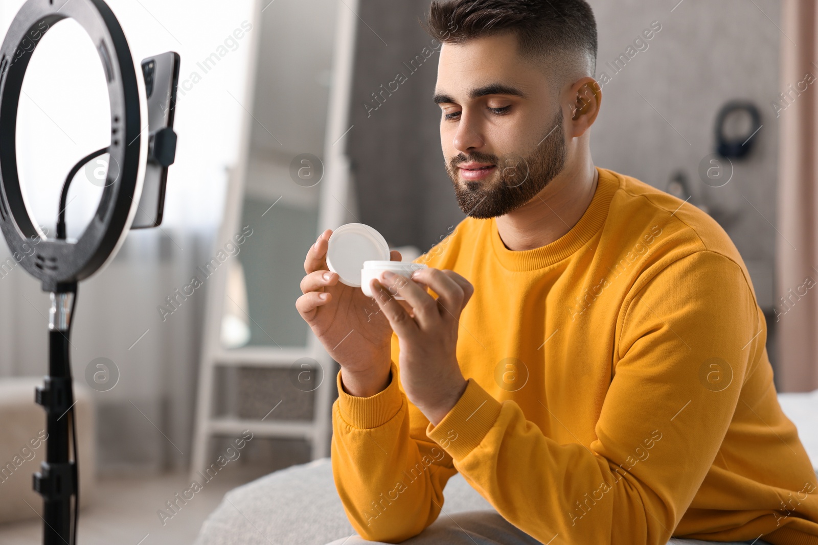 Photo of Beauty blogger reviewing cosmetic product and recording video with smartphone and ring lamp at home