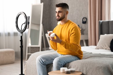 Photo of Beauty blogger reviewing cosmetic product and recording video with smartphone and ring lamp at home