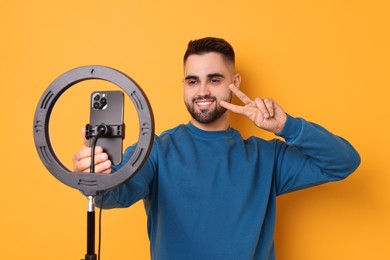 Blogger recording video with smartphone and ring lamp on orange background