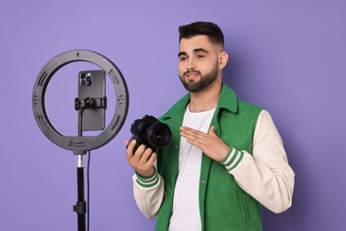 Photo of Technology blogger reviewing camera and recording video with smartphone and ring lamp on purple background