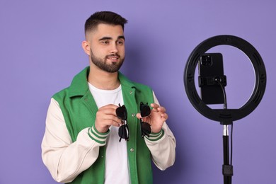 Photo of Fashion blogger reviewing sunglasses and recording video with smartphone and ring lamp on purple background