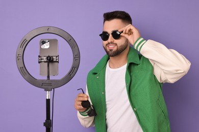 Fashion blogger reviewing sunglasses and recording video with smartphone and ring lamp on purple background