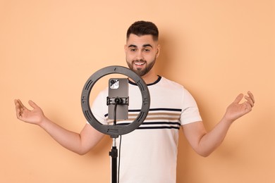 Blogger recording video with smartphone and ring lamp on beige background