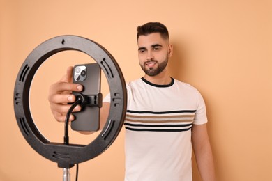 Blogger recording video with smartphone and ring lamp on beige background