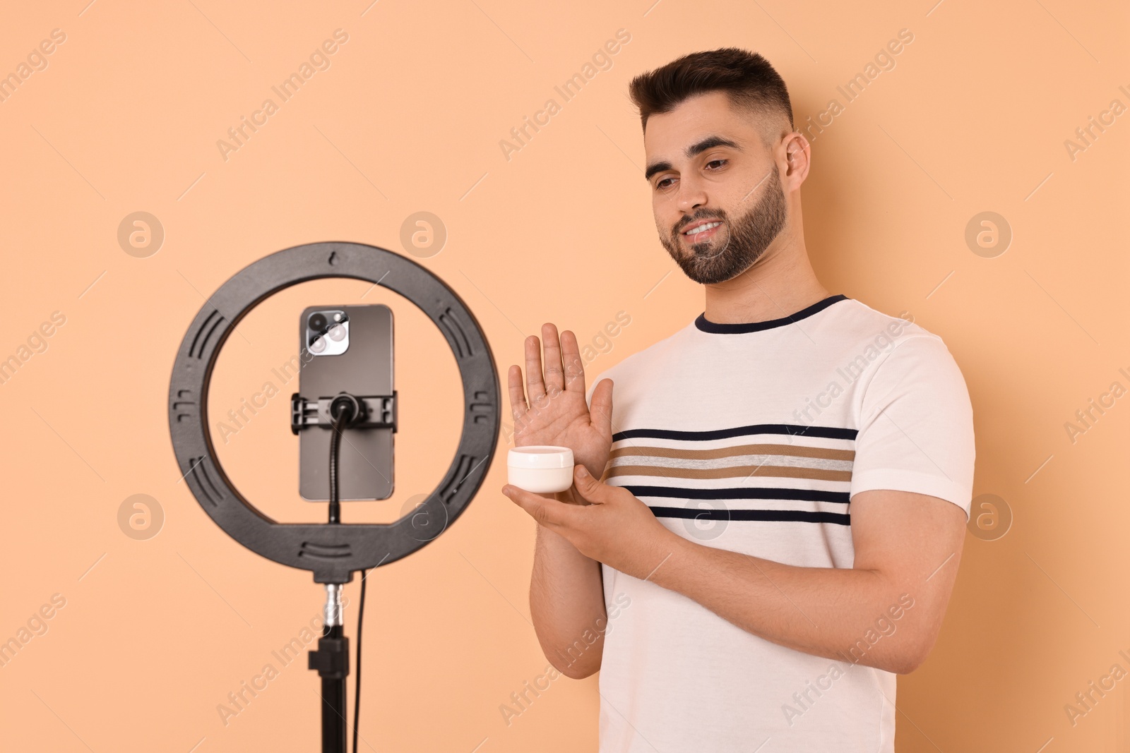 Photo of Beauty blogger reviewing cosmetic product and recording video with smartphone and ring lamp on beige background