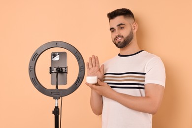 Beauty blogger reviewing cosmetic product and recording video with smartphone and ring lamp on beige background