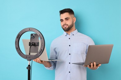 Photo of Technology blogger reviewing laptops and recording video with smartphone and ring lamp on light blue background
