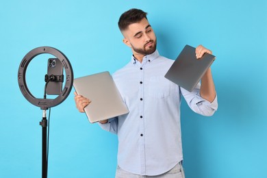 Technology blogger reviewing laptops and recording video with smartphone and ring lamp on light blue background