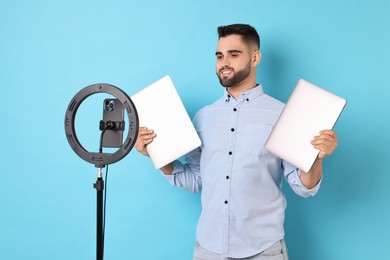 Technology blogger reviewing laptops and recording video with smartphone and ring lamp on light blue background