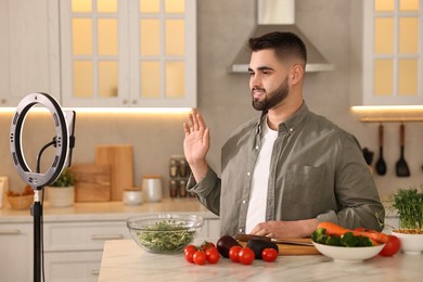 Food blogger cooking while recording video with smartphone and ring lamp in kitchen