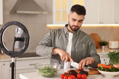 Photo of Food blogger cooking while recording video with smartphone and ring lamp in kitchen