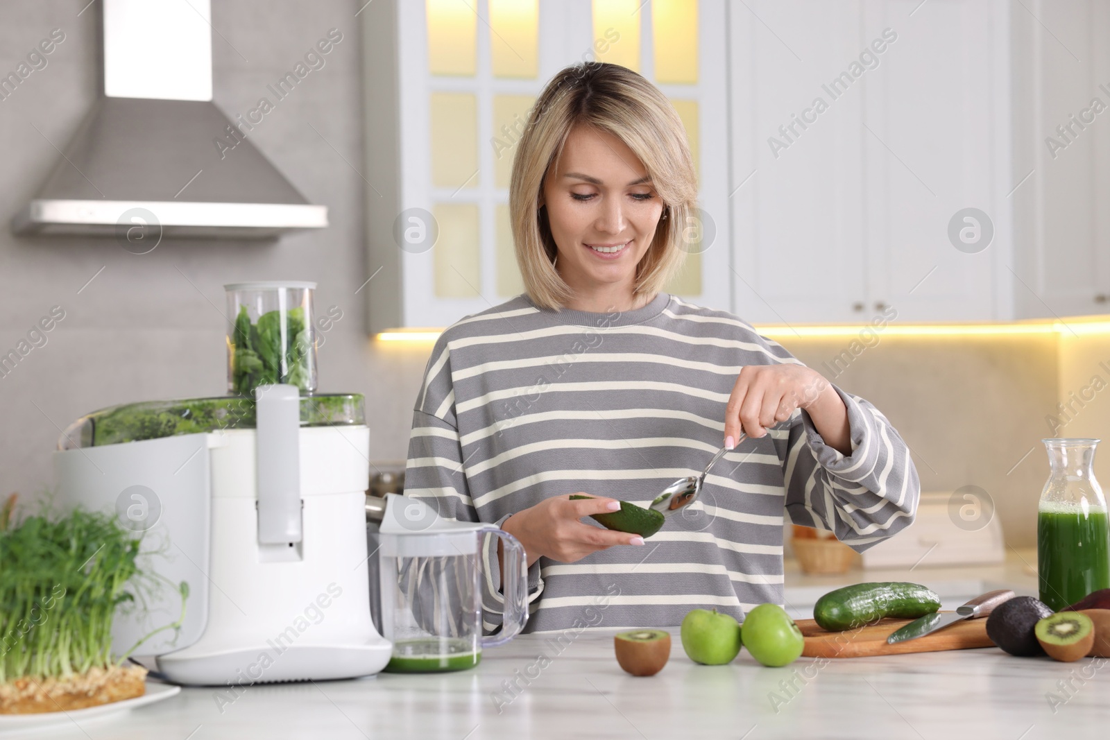 Photo of Smiling woman with fresh products using juicer at white marble table in kitchen