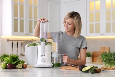 Smiling woman with fresh products using juicer at white marble table in kitchen