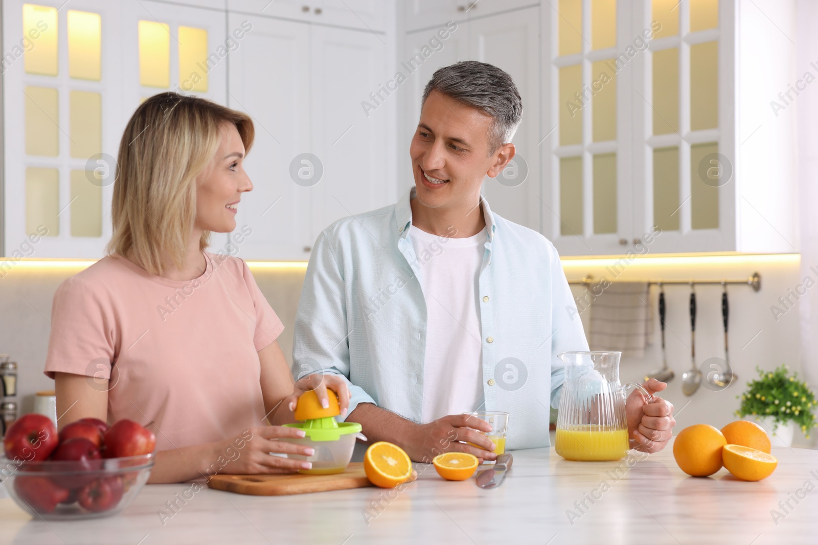 Photo of Happy couple with juicer and fresh products making juice at white marble table in kitchen