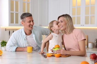 Photo of Happy family with juicer and fresh products making juice at white marble table in kitchen